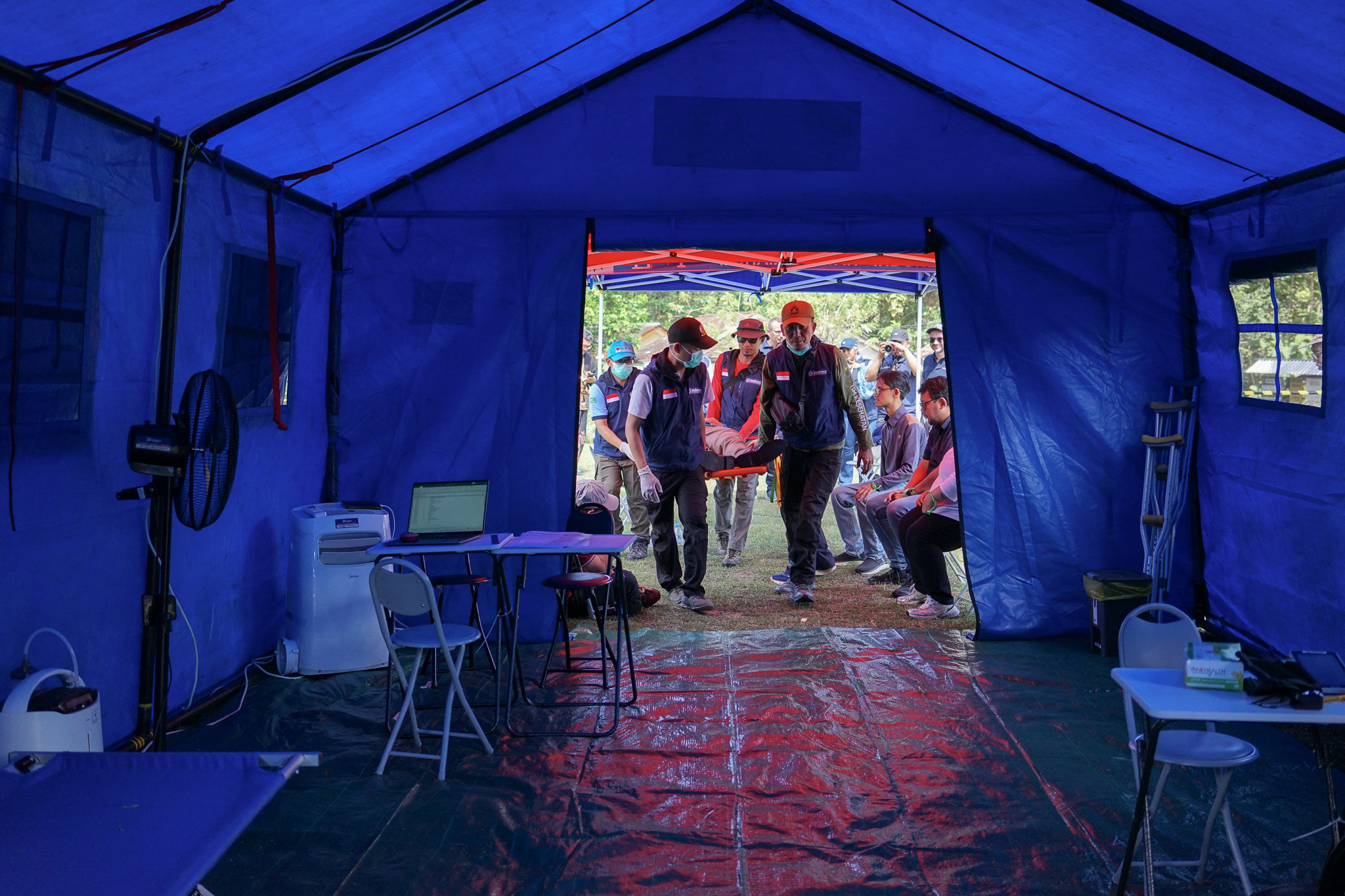 Interior of blue emergency tent with medical equipment, rescue team members gathered at entrance